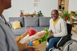 © AnnaStills - African happy man with disability sitting in wheelchair and meeting caregiver bringing groceries for him