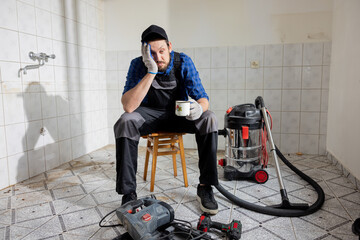 Wall Mural - A sad man tired of construction finishing work at home sits with head bowed leaning his hand against cheek. The man drinks coffee to wake up gathers strength to continue working.