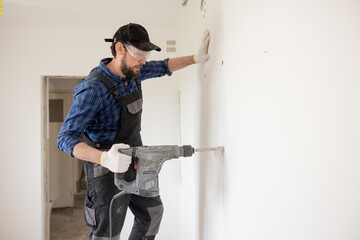 Wall Mural - Portrait of a young man with an electric drill and making a hole in the wall. Interior design and home renovation concept.