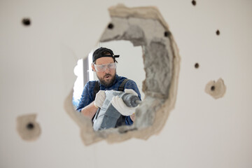 Poster - Demolition of an old house. Demolition of unnecessary walls with hand-held impact hammer. A view of an experienced construction worker trying with all might to enlarge hole in wall.