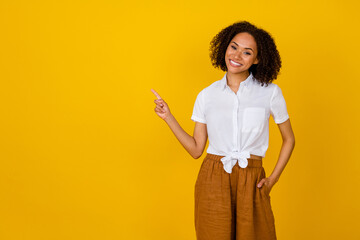 Poster - Photo of positive cheerful funky girl curly hairstyle white blouse directing empty space hand pocket isolated on yellow color background