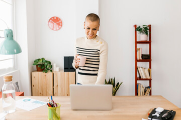 Mid adult business woman reading email on laptop in the morning while drinking coffee at home office