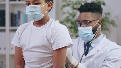 Wall Mural - Pediatrician examining sick black boy in medical face mask to diagnose disease