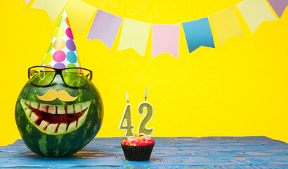 Funny watermelon in festive garlands for happy birthday greetings funny. Copy space watermelon with smile character. Happy birthday with number 42.