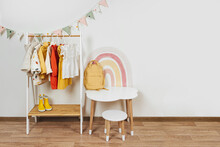 Children's Room With Montessori Clothing Rack, White Table And Rainbow. Dress, Jacket And Sweaters On Hangers In Wardrobe. Nursery Storage Ideas. Montessori Toddler Room