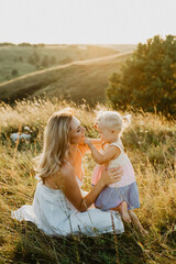 A beautiful young mother with a little daughter are hugging and walking across the field at sunset.