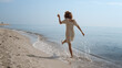 Leinwandbild Motiv Cheerful girl running ocean waves back view. Playful woman walking wet sand.