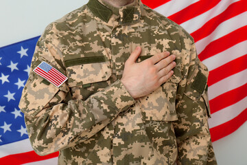 Wall Mural - Soldier holding hand on heart near United states of America flag on white background, closeup