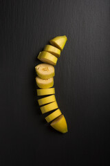 Wall Mural - sliced fresh ripe banana, harvested tropical fruit on black textured background, taken from above with space for text