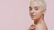 © pavel_dp - Cute slim young Caucasian half-turned woman with light hair strokes her clavicle looking at the camera over her nude shoulder on pale pink background | Body care concept