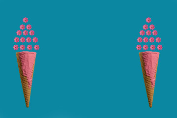 Two ice cream cones decorated with pink flowers. Isolated on blue background. Minimal concept. Flat lay.