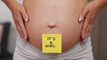 It's A Girl. Yellow Sticker Stuck To A Big Pregnant Belly Of A Caucasian Woman With A Tattoo On Her Hand. Maternity And Parenthood Concept. High Quality 4k Footage