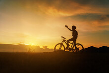 Silhouette Of Woman Riding Bicycle At Sunset, Cheerfully At The End Of The Day. Woman Riding Break Relax And Take A Photo Landscape And Looking Forward With Beautiful Nature At Sunset Time.