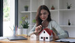 © wichayada - Happy woman hand holding magnifying glass and looking at house model, house selection, real estate concept.