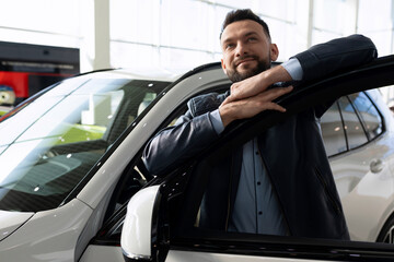 Wall Mural - a man in a car dealership dreamily hugs the door of a new car