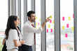 © amorn - Group of businesspeople use post it notes on glass wall. Group of corporate diverse colleagues use sticky note brainstorming and share ideas on glass wall