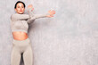 © halayalex - Fitness confident woman in sports clothing. Sexy young beautiful model with perfect body. Female posing near grey urban wall in studio. Stretching out before training