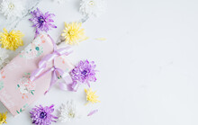 Flowers Composition With White, Purple And Yellow Chrysanthemum Flowers And Gift Box On White Marble Background.