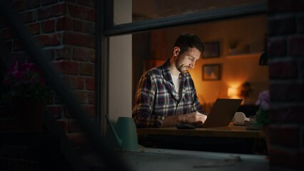 Aufkleber - Focused Man Working on a Laptop Late in the Evening Finishing Important Project at Home Office. Freelancer Working Remotely. Warm Lit Cozy Apartment. View From Outdoors into Window.