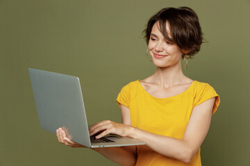 Wall Mural - Young smiling freelancer programmer happy woman she 20s wear yellow t-shirt hold use work on laptop pc computer isolated on plain olive green khaki background studio portrait People lifestyle concept