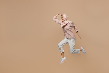 Poster - Full body fun young arabian asian muslim woman she wears abaya hijab pink clothes jump high look far away distance isolated on plain pastel light beige background. People uae islam religious concept