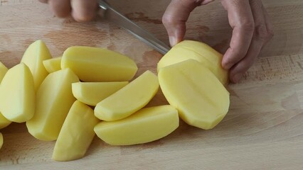 Wall Mural - Woman's hand with a knife cutting the potatoes on the wooden board in the kitchen. Healthy eating and lifestyle.