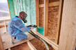 Male builder insulating wooden frame house. Man worker spraying polyurethane foam inside of future cottage, using plural component gun. Construction and insulation concept.