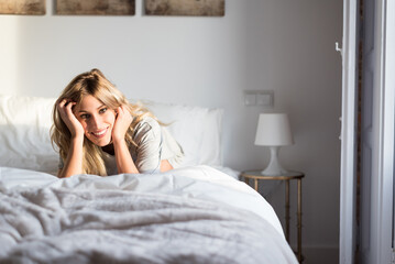 happy beautiful young woman smiling on bed looking at camera