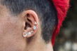 Closeup of a female punk's ear with silver piercings and a bright red dyed mohawk personal hair style