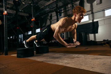 Wall Mural - Portrait of young sportive man with muscular body training, doing push-ups exercises isolated over geym background. In the air