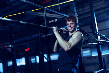 Wall Mural - Portrait of sportive muscular young man training, doing pull up exrcises isolated over gym background. Developing strength.