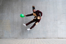 Playful Man With Balloon Jumping In Front Of Concrete Wall