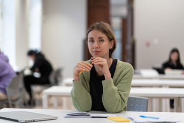 Mature students in higher education. Pensive middle-aged woman adult learner sitting at library table, preparing for exams, getting second degree, 45s female studying in classroom. Selective focus