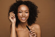Black shirtless woman with curly hair smiling and using mascara