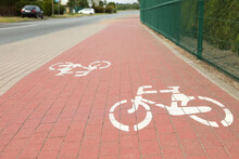 Red Bicycle Lane With White Signs On Pavement Along Road
