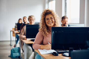 happy college student taking notes on computer class and looking at camera.