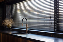 Wooden Blinds Black Color Closeup On The Window. Bamboo Slats 50mm Wide. Venetian Wood Blinds In The Kitchen. Black Tapes. Sink With Copper Faucet Near The Window. Round Vase Is On The Windowsill.