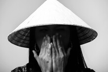 Portrait Of Asian Woman With Cone-shaped Asian Cane Hat And Costume Cover Her Face With Hands And Hiding Eyes In Shade Of Hat. Model With National Chinese Costume. Black And White Image