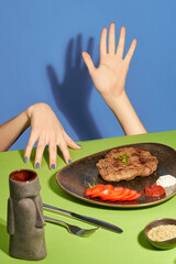 Juicy medium-rare beef steak with tomatoes on a black plate on a green table. Hands reach out to it to try the taste.