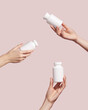 Hands holding blank white plastic tubes on pink background. Packaging for pills or capsules. Medic product branding mockup.