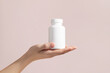 Young female hand holding blank white squeeze bottle plastic tube on pink background. Mockup.