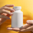 Young female hands holding blank white squeeze bottle plastic tube on yellow background. Packaging for pills, capsules or supplements. Mockup.