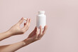 Woman holding pill and blank white plastic tube on pink background. Packaging for pill, capsule or supplement. Medic product branding mockup.
