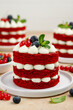 Mini red velvet cakes decorated with berries and mint. Portion cake on a white plate with. Selective focus 