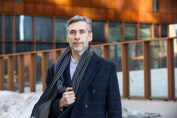 a middle-aged man with gray hair in a blue coat is standing on the street