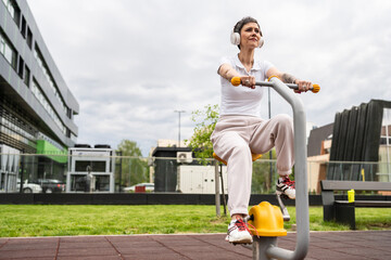 One woman modern mature caucasian female with short hair training in front of building in day on bicycle trainer machine simulator at outdoor gym Sport fitness healthy lifestyle concept copy space