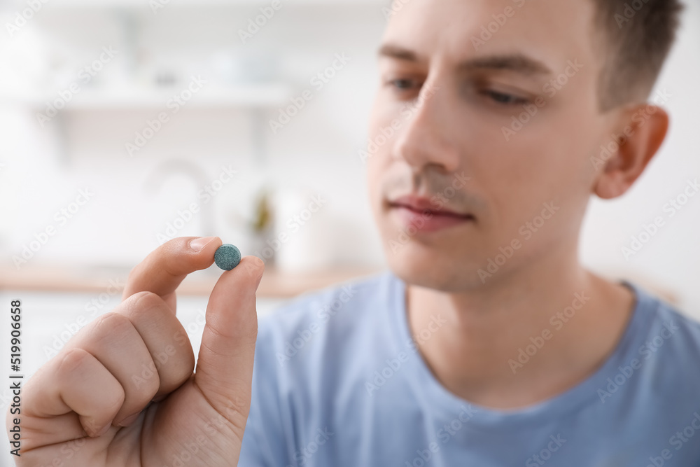 Young man with vitamin supplement at home, closeup