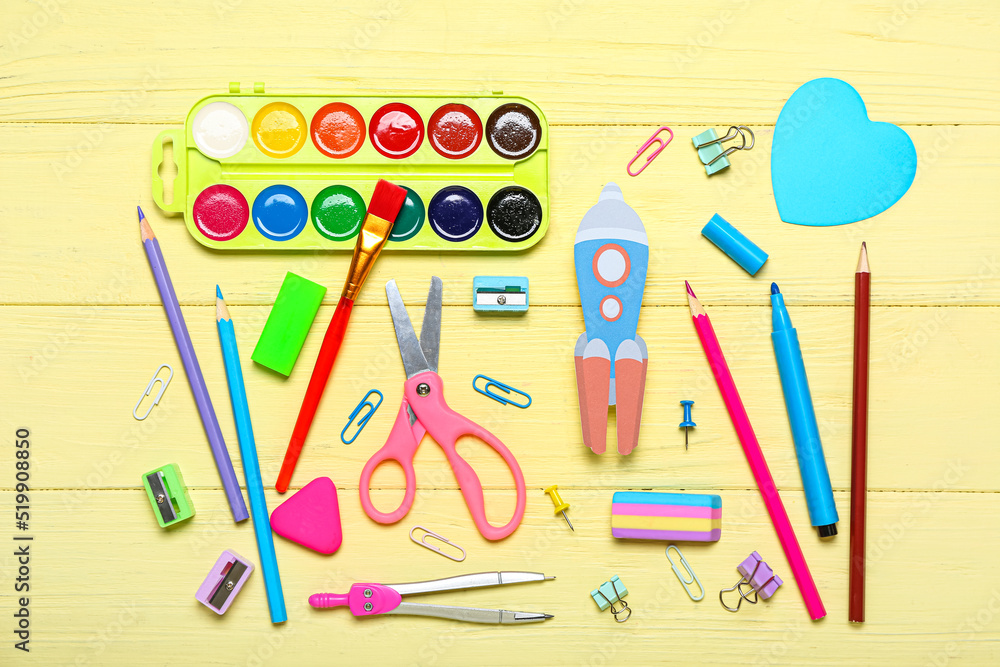 Paper rocket with school stationery on yellow wooden background
