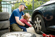 © MNStudio - Cute toddler boy helping his father to change car wheels at their backyard. Father teaching his little son to use tools.