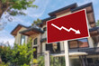 A sign showing an downward arrow in front of a house. Concept of decreasing or slumping home prices and value or a real estate bust.